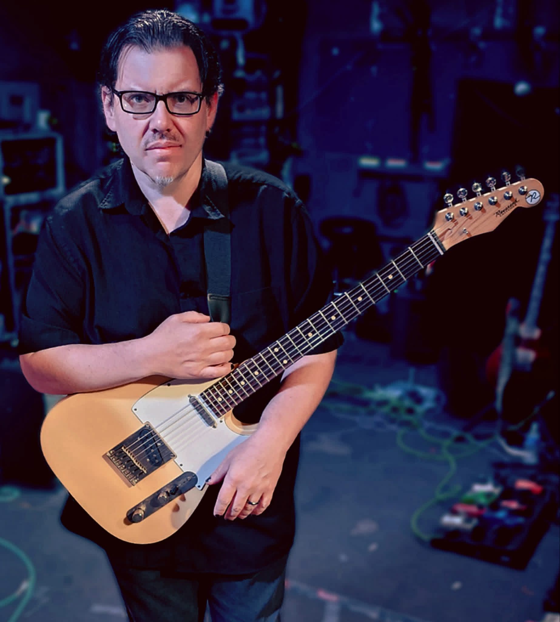 Jack Miele on stage under blue and purple lights with a blonde Reverend electric guitar