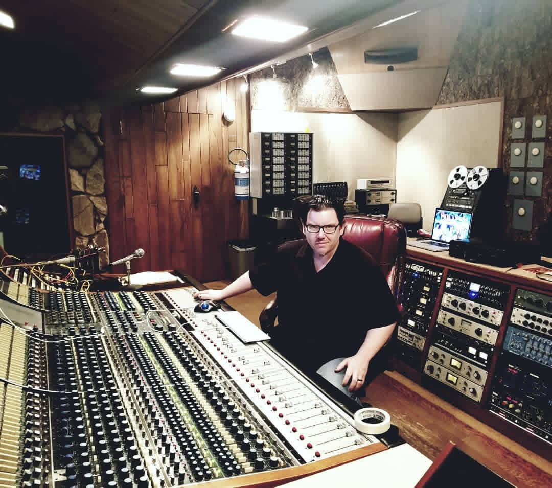 Jack Miele seated at a huge analog mixing console with reel-to-reel tape machines and outboard gear behind him