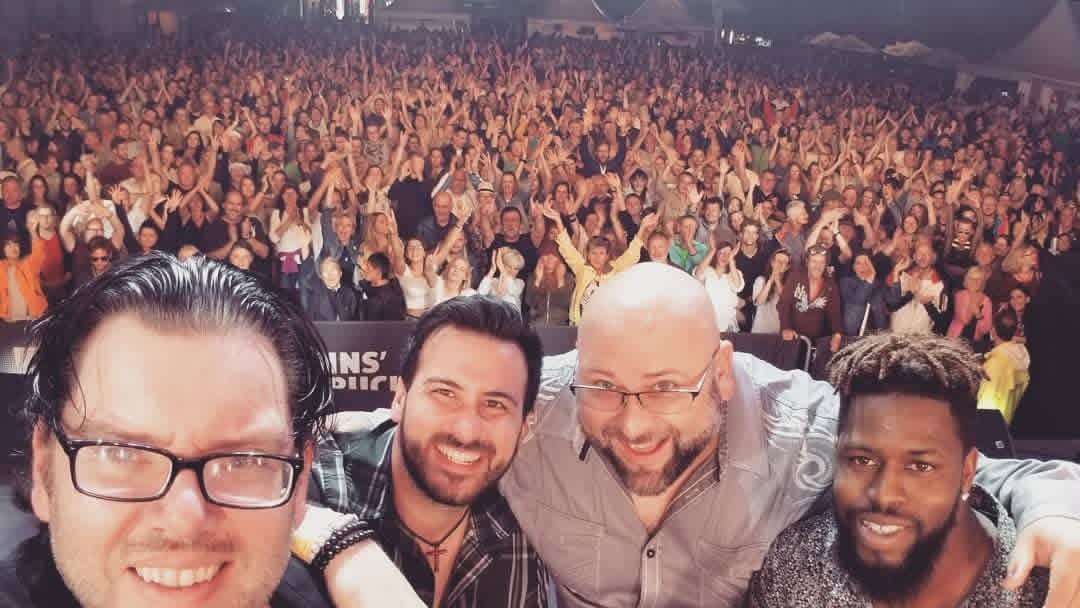 Jack Miele in a group selfie on stage in front of a huge outdoor festival crowd