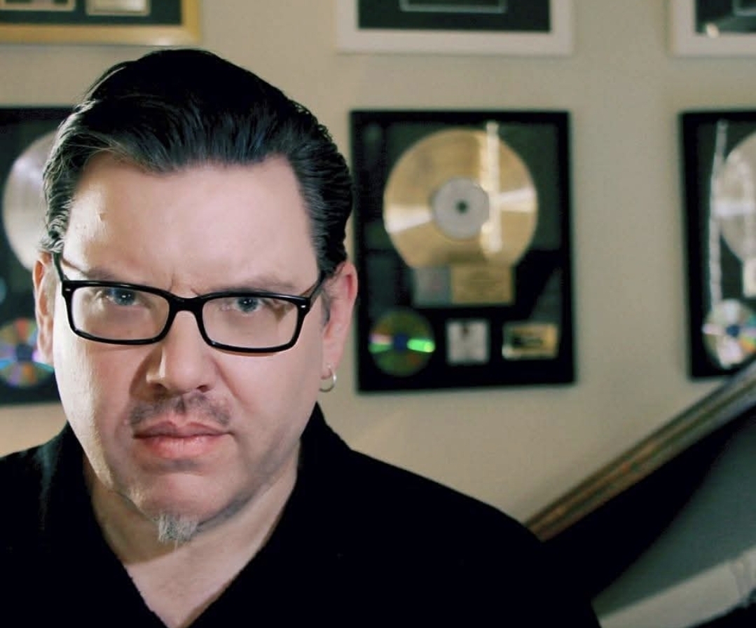 Close portrait of Jack Miele with gold records on the wall behind him